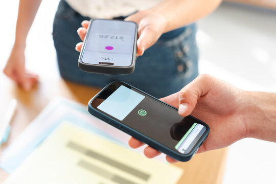 A customer pays for a purchase using a mobile device held near a business owner's smartphone, completing a secure contactless transaction in a modern retail setting.