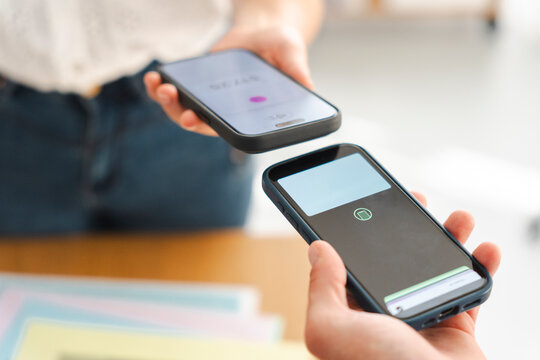 A person completes a contactless payment transaction by holding their smartphone near another mobile device held by a shop assistant to process the financial transfer.