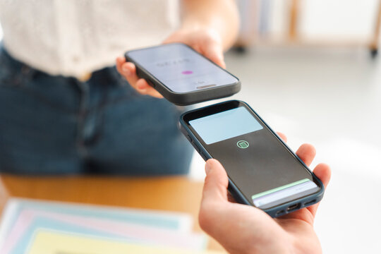 A customer pays a merchant using contactless technology by tapping their smartphone against the seller device to process a secure transaction in a retail shop.