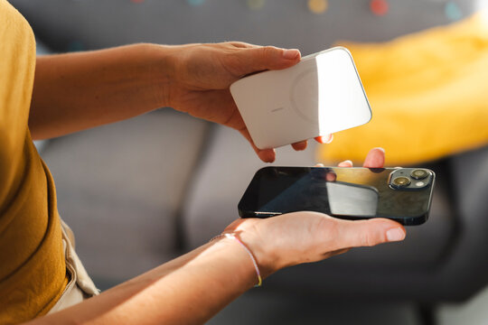 A person prepares to charge their smartphone using a magnetic wireless power bank. The device is held over the mobile phone to initiate the wireless charging process.
