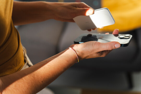 A person prepares to attach a wireless portable charger to the back of their smartphone. This device allows for convenient power delivery without any messy cables.