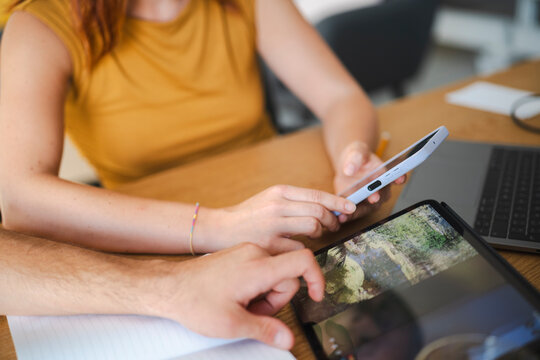 A woman and a man work together at a desk, using a smartphone and a tablet to review images. The professional team collaborates on a creative project in an office.