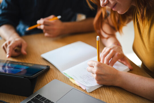 A man and a woman work together at a table. The woman writes in a notebook while the man looks at a tablet during their collaborative project session in an office.