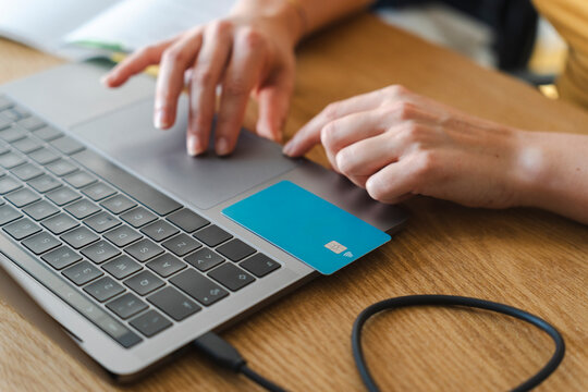 A person uses a laptop to make an online payment. A blue debit card is placed on the trackpad while their hands navigate the keyboard to complete the digital purchase.
