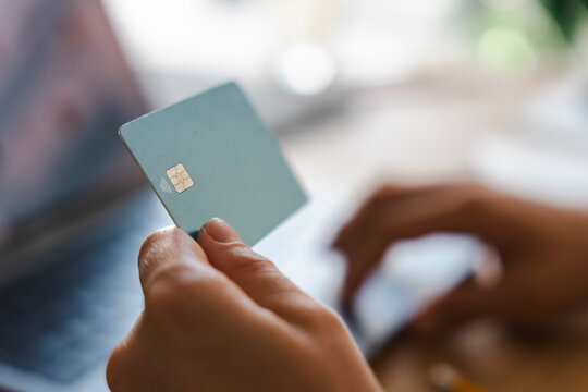 A person is holding a credit card while sitting in front of a laptop computer. They are performing an online transaction to make a secure payment from their home office.