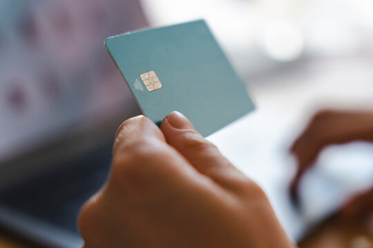 A person is holding a plastic payment card in front of a laptop computer. They are engaged in online shopping and entering financial information for a secure purchase.