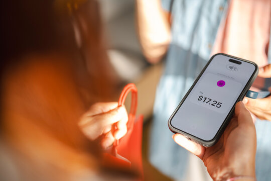 A customer uses a mobile phone to complete a contactless payment for a shopping purchase. The digital wallet screen shows a transaction total of seventeen dollars.