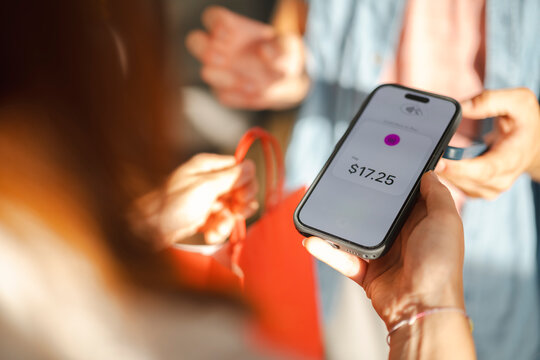 A customer uses a mobile phone to complete a contactless transaction for seventeen dollars and twenty-five cents. They hold a shopping bag during the checkout process.