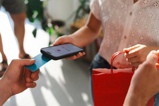 A customer makes a purchase by tapping their credit card onto a mobile payment device held by a shop assistant. The transaction takes place in a brightly lit store.