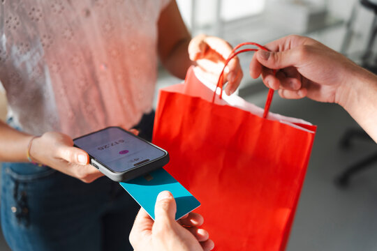 A customer pays with a credit card on a mobile phone terminal while receiving a red shopping bag from a clerk. This transaction depicts a simple modern purchase.