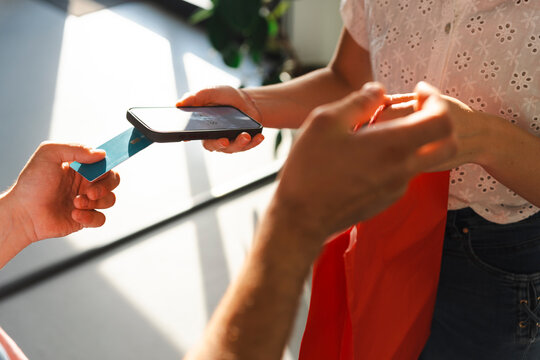 A customer completes a transaction by tapping their credit card on a handheld mobile payment device. This demonstrates a modern contactless purchase in a retail shop.