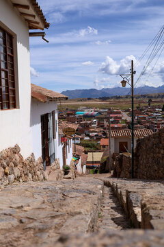 Cusco, Peru - 18 May 2022: View of the historic town of Chinchero with its traditional stone-paved streets, white adobe buildings, and distant Andean mountains under a bright blue sky.