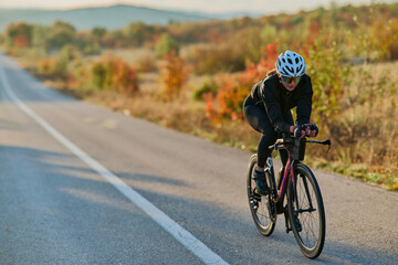 Fototapeta premium Female Cyclist Training On Road Bike Through Autumn Countryside At Sunrise Fitness Ride