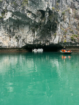 Vietnam - 17 August 2026: View of a small boat with tourists in orange life vests rowing through a limestone cave in the turquoise waters of Ha Long Bay.