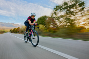 Fototapeta premium Female Road Cyclist Riding Fast On Open Road At Sunset With Motion Blur And Athletic Focus