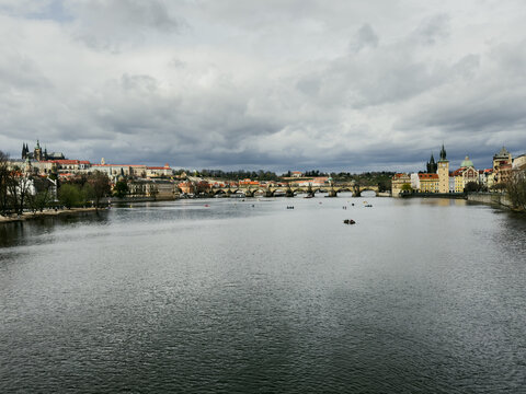 Prague, Czechia - 17 August 2026: View of Charles Bridge spanning the Vltava River with historic buildings and spires under a cloudy sky.