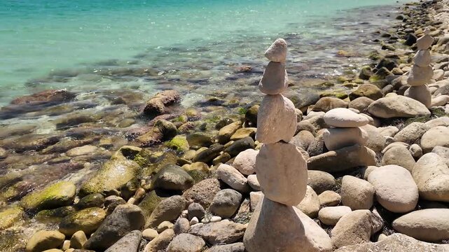 Balanced stone towers rise from a pebble beach beside clear turquoise water, evoking calm and mindfulness ideal footage for wellness and meditation content