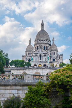 Looking up at exterior of the sacre-coeur basilica in Paris city centre, France in summer with clear blue skies overhead and trees around below the cathedral church with dome and spire