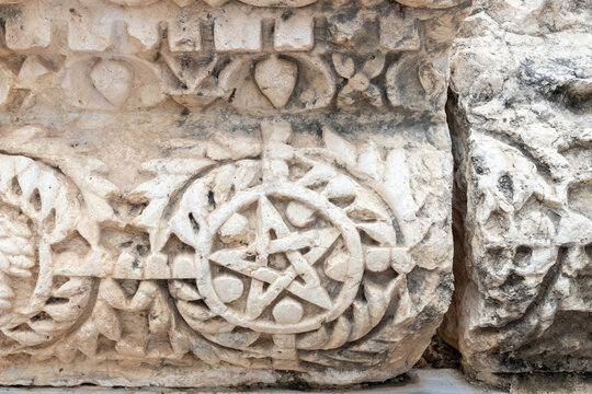 Capernaum, North District, Israel - 08 March 2015: View of an ancient stone carving featuring a pentagram symbol within a wreath, located among the archaeological ruins of the historic synagogue.