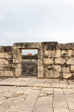 Capernaum, Israel - 08 March 2015: View of the ancient stone ruins and doorway in Capernaum with the red dome of the Greek Orthodox Church visible in the background.