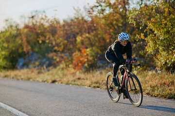 Fototapeta premium Female Cyclist Training on a Road Bike in Autumn Countryside Wearing Helmet and Sunglasses