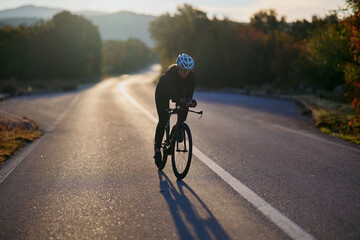 Fototapeta premium Female Cyclist Training On Empty Country Road At Sunrise With Helmet And Racing Bike