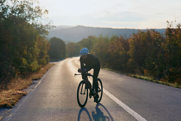 Fototapeta premium Solo Road Cyclist Training At Sunrise On Quiet Rural Road Through Autumn Countryside