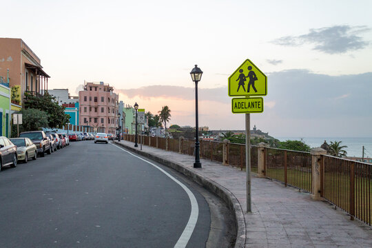 San Juan, San Juan, Puerto Rico - 22 March 2014: View of historic Viejo San Juan streets with colorful colonial buildings, a pedestrian crossing sign, and the coastline at sunset.