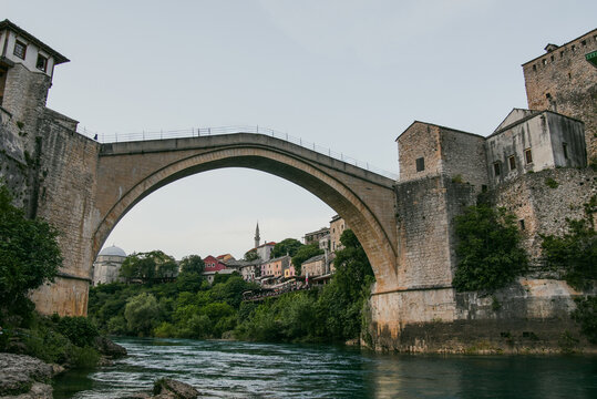 Mostar, Bosnia and Herzegovina - 16 August 2026: View of Stari Most, the iconic stone arch bridge spanning the Neretva River, surrounded by historic stone buildings and lush greenery.