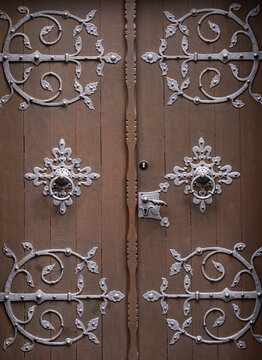 Metal design on historic wooden doorway. Metal design with weathered iron texture. Antique ornamental metal design around door knocker. Architectural detail with metal design and patina.