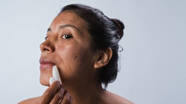 Portrait of young Hispanic woman massaging face with gua sha stone. Clip is ideal for skincare brands, beauty tutorials, and wellness marketing campaigns
