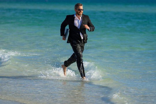 Excited summer business travel. Freelance work, online working. Summer businessman in suit run in sea water. Freelance travel. Funny freelancer in suit jump and run in the sea. Freelance and holidays.