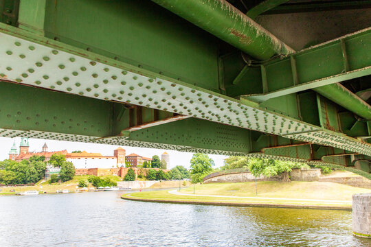 A close-up view of a large, painted green steel plate bridge seen from a boat passing beneath it. with rows of structural rivets. A view from astern to the churned-up water and the green riverbanks. 