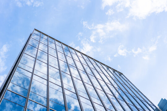 Low angle view of modern glass office building facade reflecting cloudy sky in Fukuoka, Japan