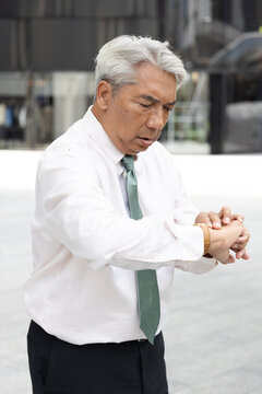 asian senior businessman looking at his wristwatch outdoors in the city, stressed about running late for an appointment