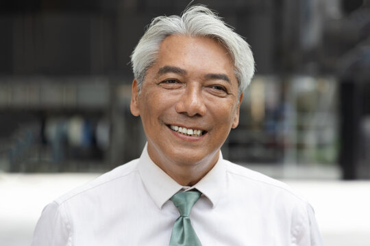 happy smiling southeast asian senior businessman portrait outdoors in the city during daytime, confident and professional