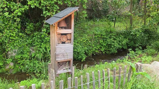 Insect house made of natural materials, set against a backdrop of a river and forest.