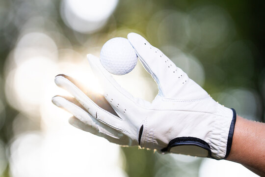 Golf ball in golf glove. Golfer holds white ball. Hand holding golf ball. Outdoor golf preparation.