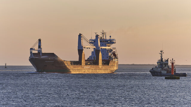 Esbjerg, Denmark - 28 July 2026: View of the cargo vessel Pietersgracht assisted by a Svitzer tugboat returning to port, with offshore wind energy infrastructure in the golden hour light.