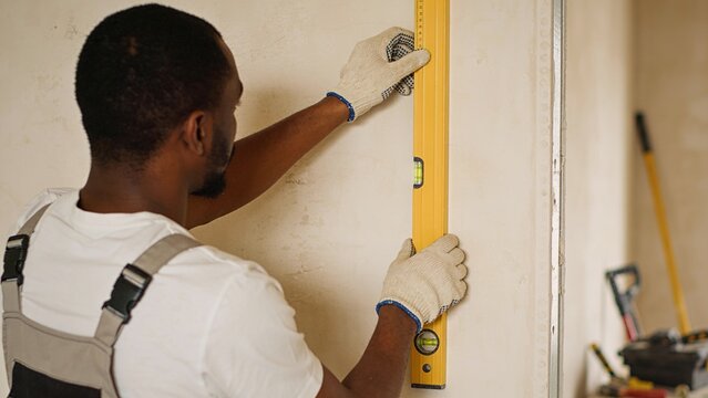 Professional construction worker measuring unfinished wall using yellow spirit level during interior renovation Skilled tradesman wearing protective gloves carefully checks horizontal alignment across
