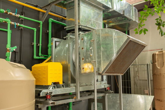 Large industrial ventilation blower and metal ductwork system with green pipes and filter unit inside building, HVAC infrastructure concept