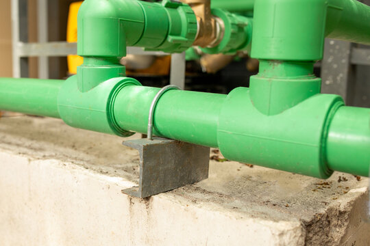 Green PVC pipes joined with support bracket mounted on concrete base outdoors, plumbing infrastructure detail