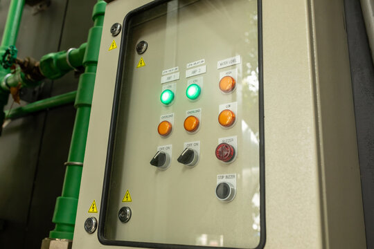 Close-up of industrial electrical control panel showing indicator lights, switches and warning labels behind glass door, automation equipment concept