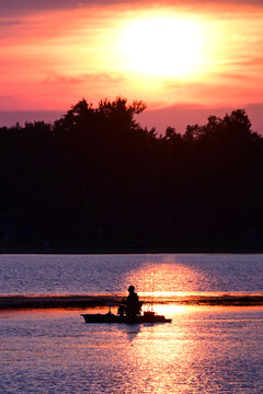 A lone fishermen sitting on a platform boat fishing boat as the sun sets behind him