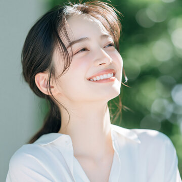 きらめく白い肌と爽やかな笑顔の日本人女性。みずみずしい緑の自然の背景。美容、スキンケア、オーラルケア、デンタルケア素材