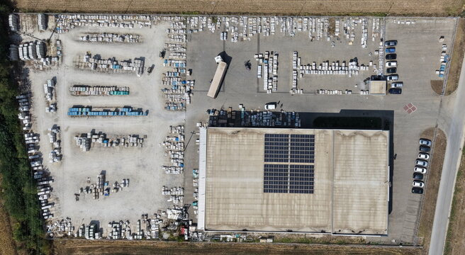 Aerial view of a cardboard and paper factory with a warehouse, rooftop solar panels, and an outdoor storage yard filled with stacked materials in Lapovo, Sumadija District, Serbia.