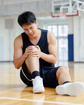 Basketball player clutching knee in pain after sports injury on gym court