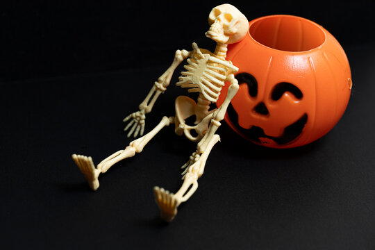 Plastic skeleton leaning on a plastic pumpkin against black background The Concept of halloween and horror