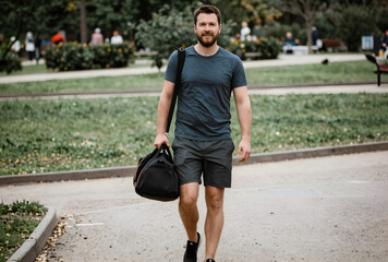 Naklejka premium Fitness and healthy lifestyle, man walking with gym bag in a park, active living and wellness journey