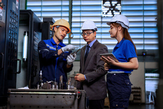 Asian factory manager and engineer team inspecting machine components with digital tablet in plant	

